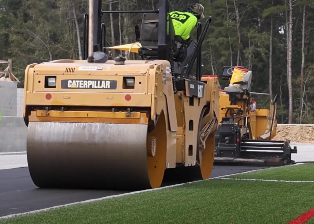 Running track installation crew utilizing machinery to finalize the sports track.