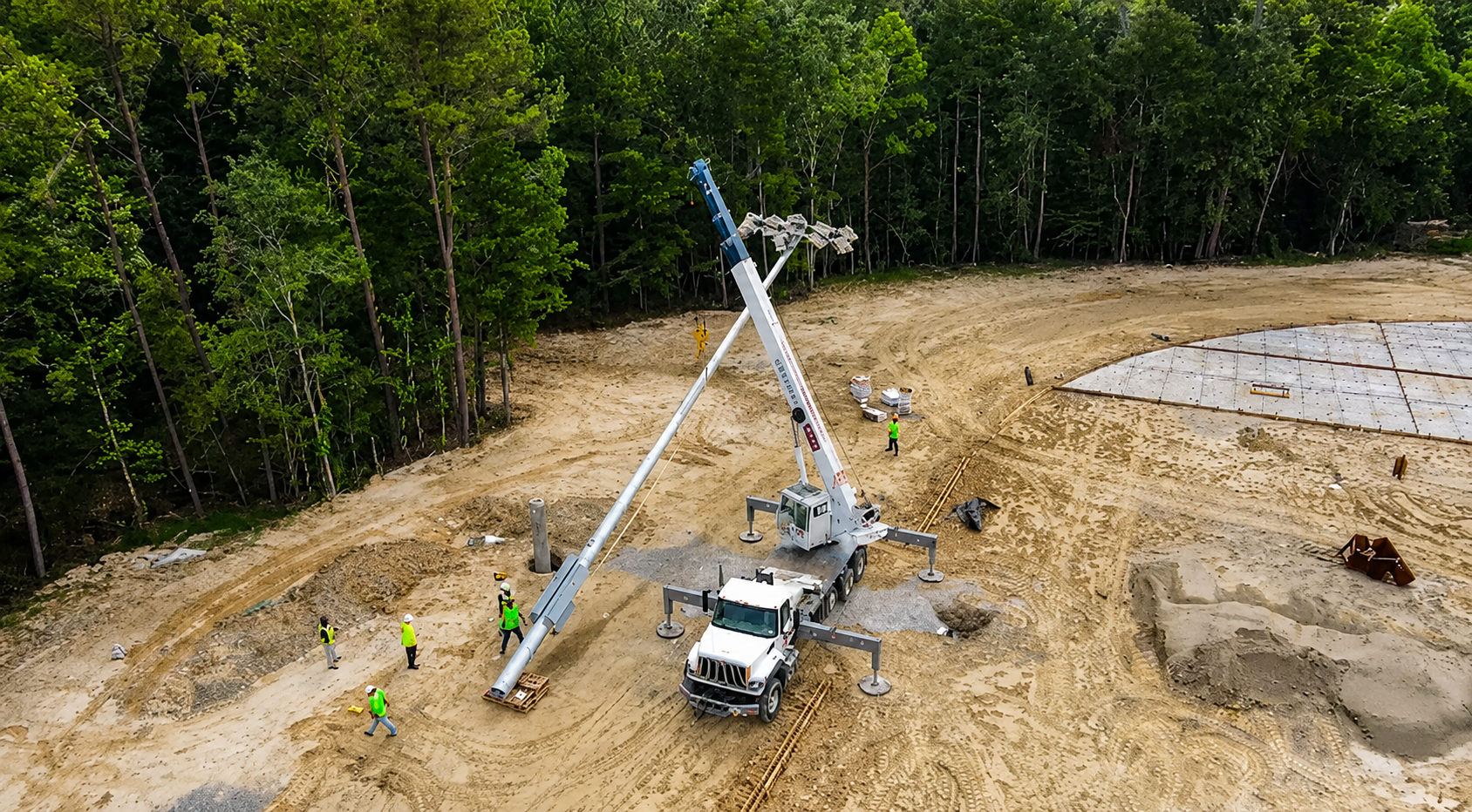 T3 Global Projects construction crew using a crane for sports lighting installation during the construction of a new artificial turf baseball field.